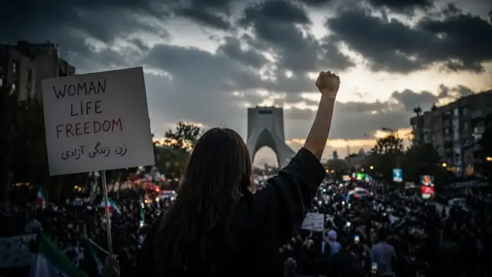 Θεσμική κινηματογραφική εικόνα διαδήλωσης στο Ιράν με σύνθημα Woman Life Freedom και πλήθος πολιτών απέναντι στο καθεστώς